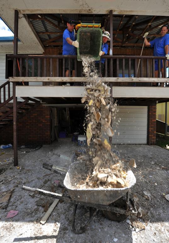 Global Care Volunteers Craig Knowles of Horsley, Reg Potter of Oak Flats and Jason Howe of Kanahooka dispose of wet gyprock stripped from the framework of a house in North Booval, Queensland.