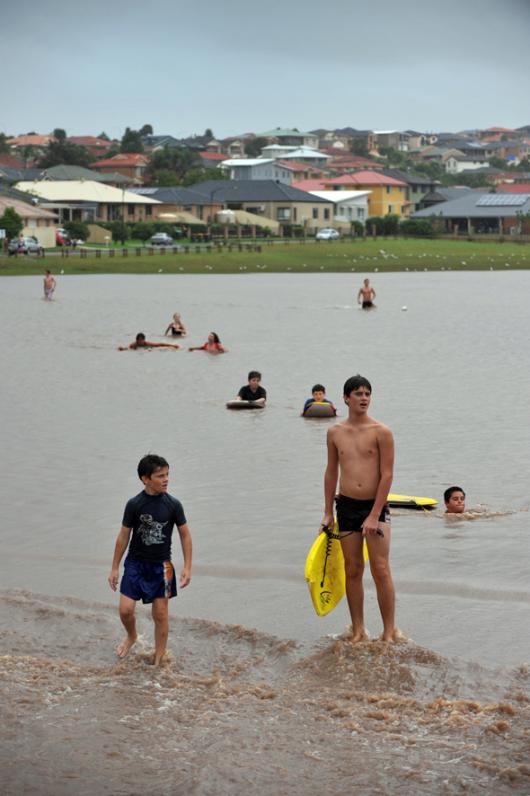 Youth frolick with body boards in the floodwaters across Flinders sporting field during flash flooding across the Illawarra region.