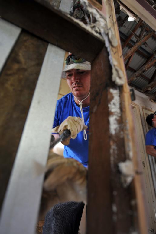 Global Care Volunteer Reg Potter of Oak Flats, strips away gyprock leaving only the framework of a house in North Booval, Queensland.