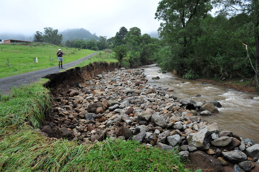 Michael Brennan stands on Daltons Road, which has been partly washed away after a recording of 286mm of rain at his property (behind) on monday.